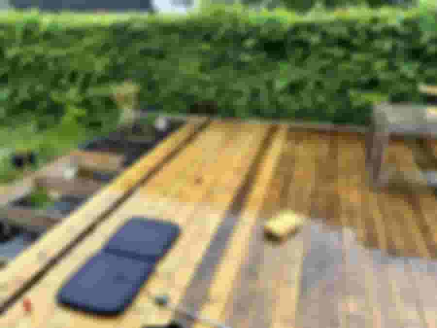 Nyrenoverad altan med träplankor, en svart sittdyna och växtbädd. Grön häck i bakgrunden ger en avkopplande atmosfär.