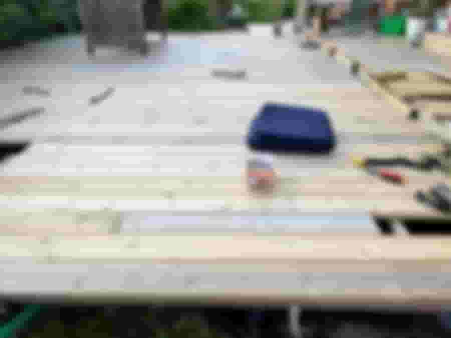 Nyrenoverad altan med träplankor, ett sittunderlag och verktyg synliga. En inbjudande utomhusmiljö som förbereds för avkoppling.