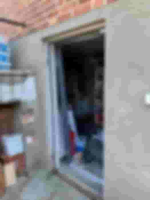 Öppen dörr till en renoveringsplats med synliga byggmaterial och verktyg. En oorganiserad arbetsyta med förvaringshyllor i bakgrunden.