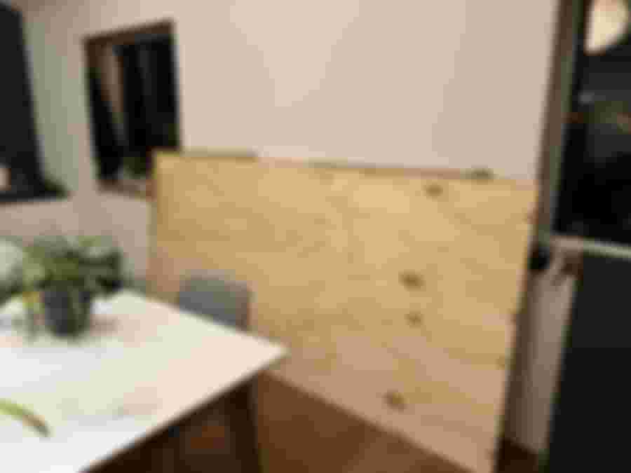 En stor plywoodskiva står lutad mot väggen i ett rum med en matta och en stol i bakgrunden.