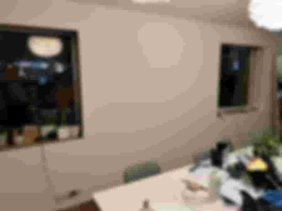 En renoverad vägg med två fönster, omgiven av en enkel inredning och en vit matta. Stämningsfull belysning och växter i fönstren.