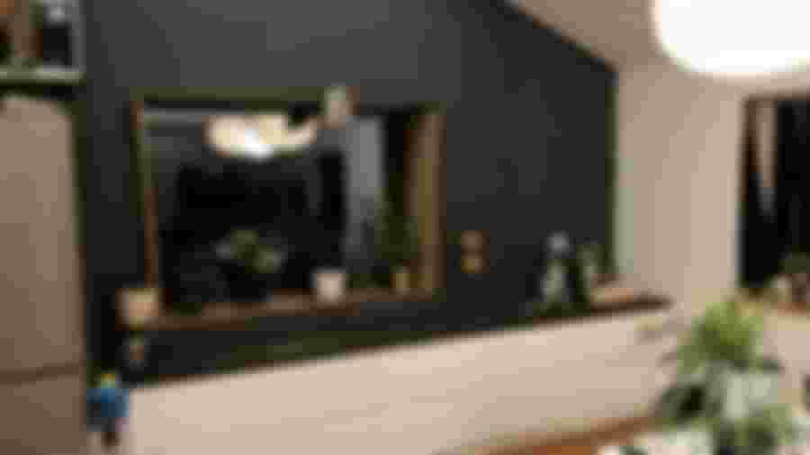 Modernt kök med svart vägg, vit köksinredning och en stor fönsteröppning. Grönskande växter och stilren belysning skapar en inbjudande atmosfär.