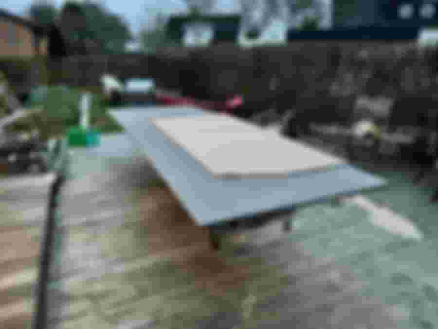 En stor arbetsyta av trä med en platta i mitten, omgiven av verktyg och trädgårdsmöbler, förberedd för renoveringsprojekt.