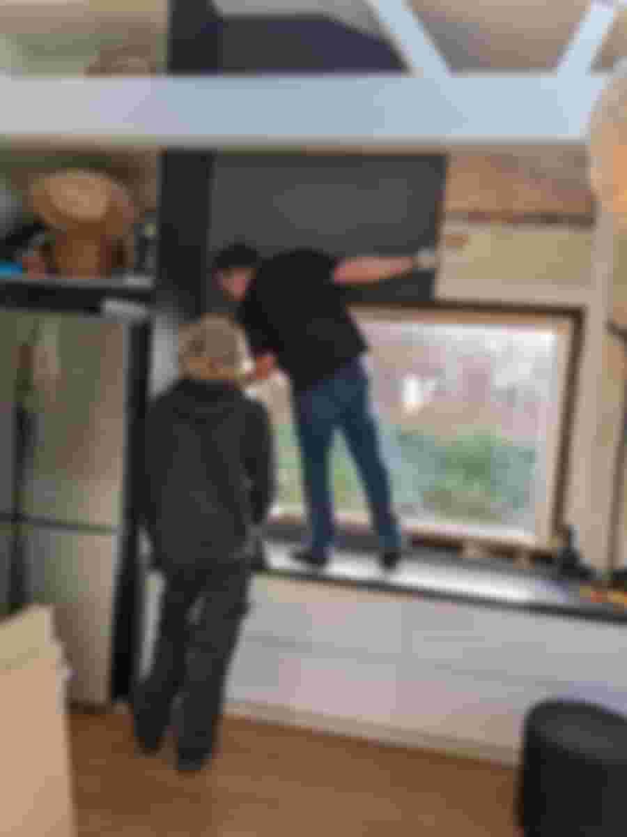 Två personer arbetar med att renovera ett fönster i ett kök, med fokus på att installera en ny fönsterbräda.