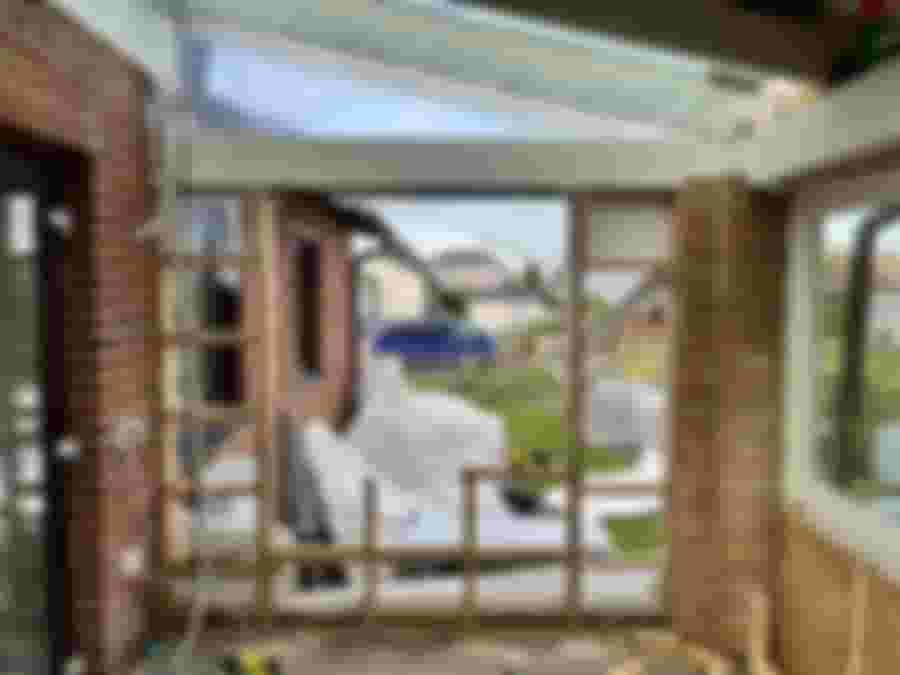 En pågående renovering visar en öppen vägg med byggställning och plastskydd. Utsikt mot en trädgård med material och verktyg synliga.