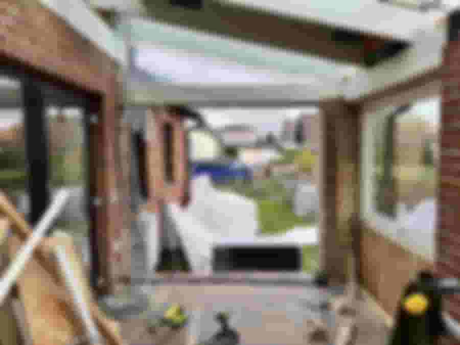 En pågående renovering av en glasveranda, med synliga byggmaterial och en öppen vy mot trädgården. Det finns verktyg och maskiner synliga.