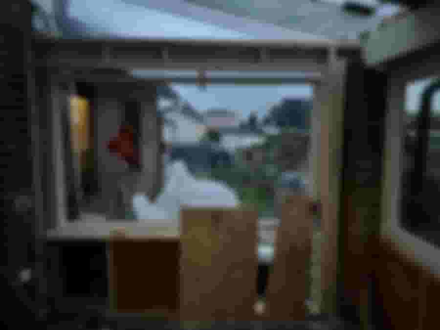 En pågående renovering av ett fönsterparti, med utsikt mot en trädgård och byggmaterial synligt inuti rummet.