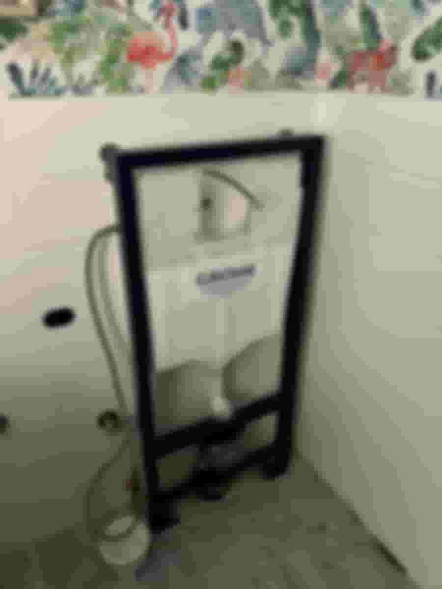 Väggmonterad toalettinstallation med Grohe-cistern, omgiven av tropiskt mönstrad tapet och vita kakelplattor. Perfekt för en uppfriskande badrumsrenovering.