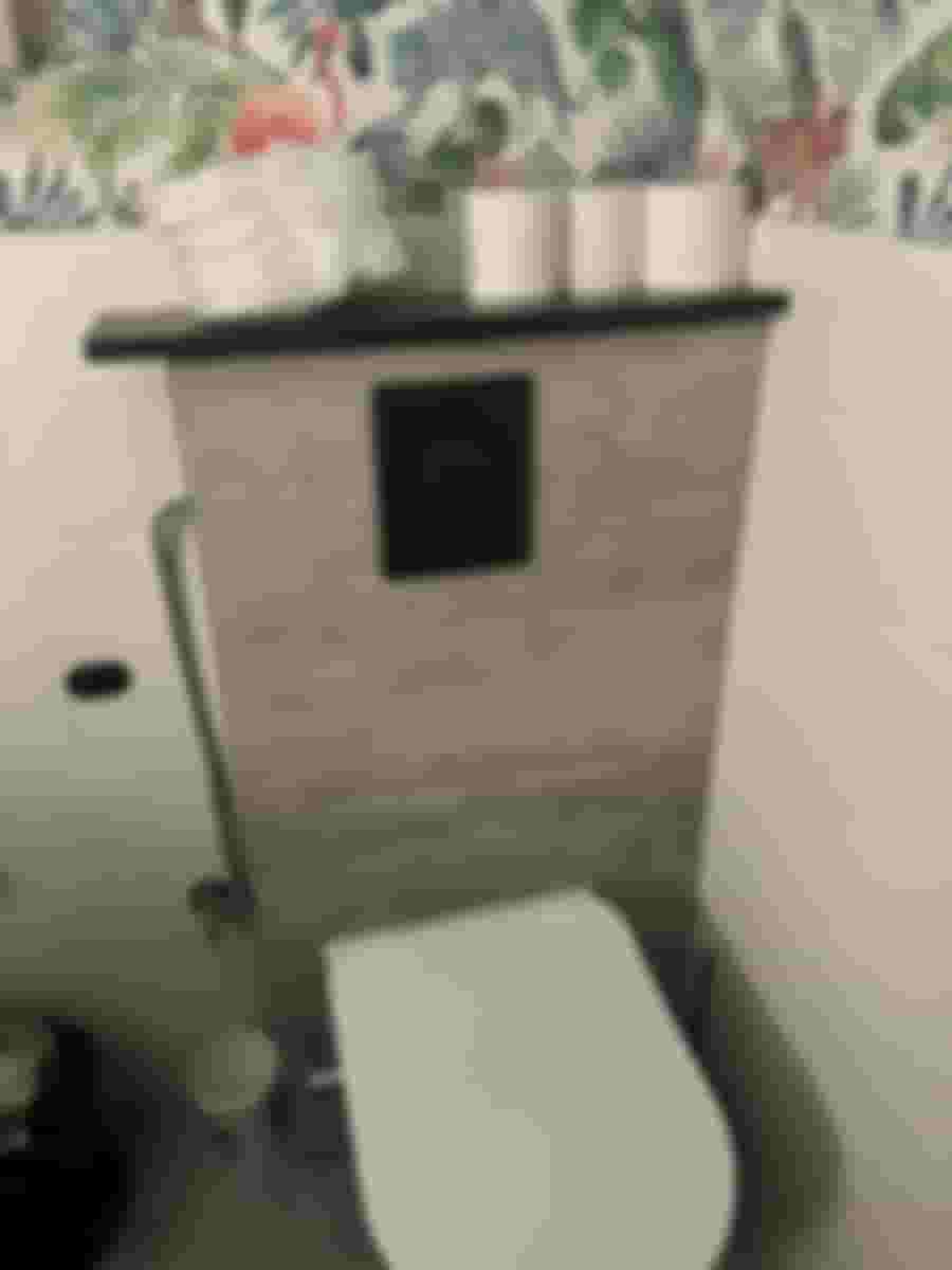 Modernt badrum med djungeltapet, väggmonterad toalett och dekorativ hylla med toalettpapper. Stilfull kontrast mellan betong och färgglada mönster.