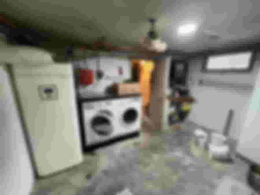 Källartvättstuga med tvättmaskin, torktumlare och förvaringshylla. Betonggolv och synliga rör. Perfekt projekt för en modern makeover.