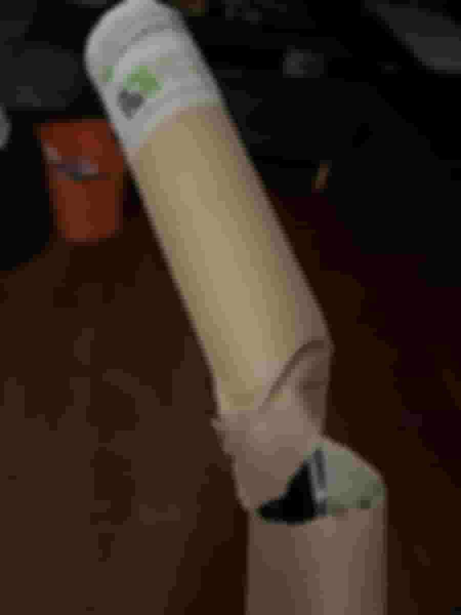 En skadad kartongtub med ett tryckt företagsemblem, delvis avslöjande innehåll. Bakgrunden visar ett mörkt rum med några möbler.