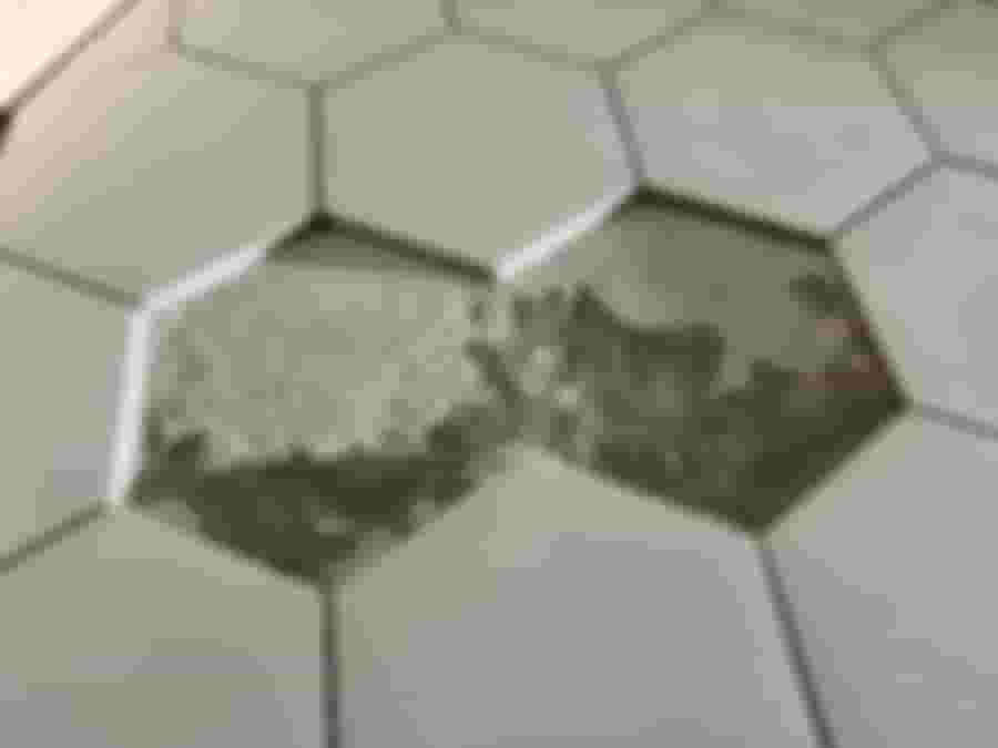 Grå hexagonala kakelplattor på golv, med ett saknat kakel avslöjande cementunderlag. Perfekt för modern renovering med geometrisk stil.