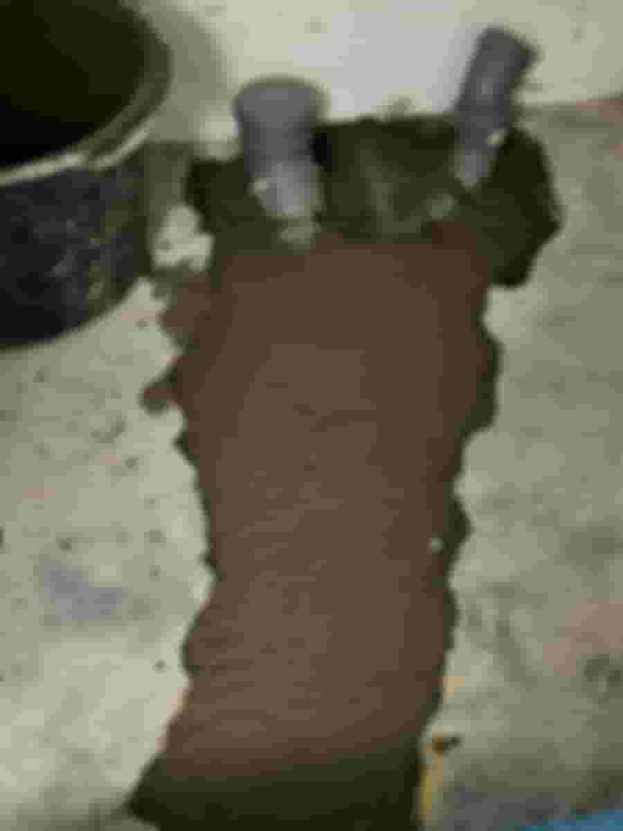 Nyinstallerade rör i ett betonggolv, omgivna av nylagd cementblandning. En hink står bredvid på det ojämna golvet.