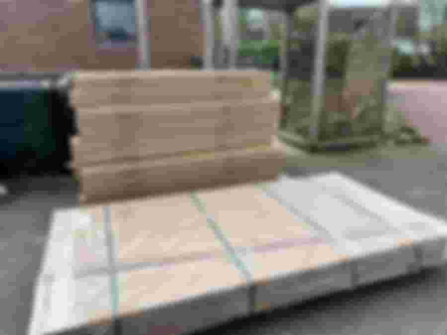 En hög med flera lådor och paket ligger staplade utomhus på marken vid en tegelbyggnad. Lådorna är märkta med "House & Wibroe Copenhagen". Det finns även en större, platt förpackning inslagen i plast och säkrad med band.