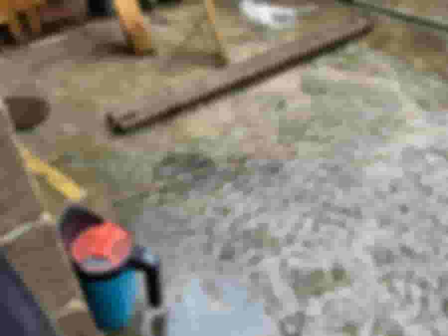 Vattensamling på golv, verktyg och skräp syns i källaren.